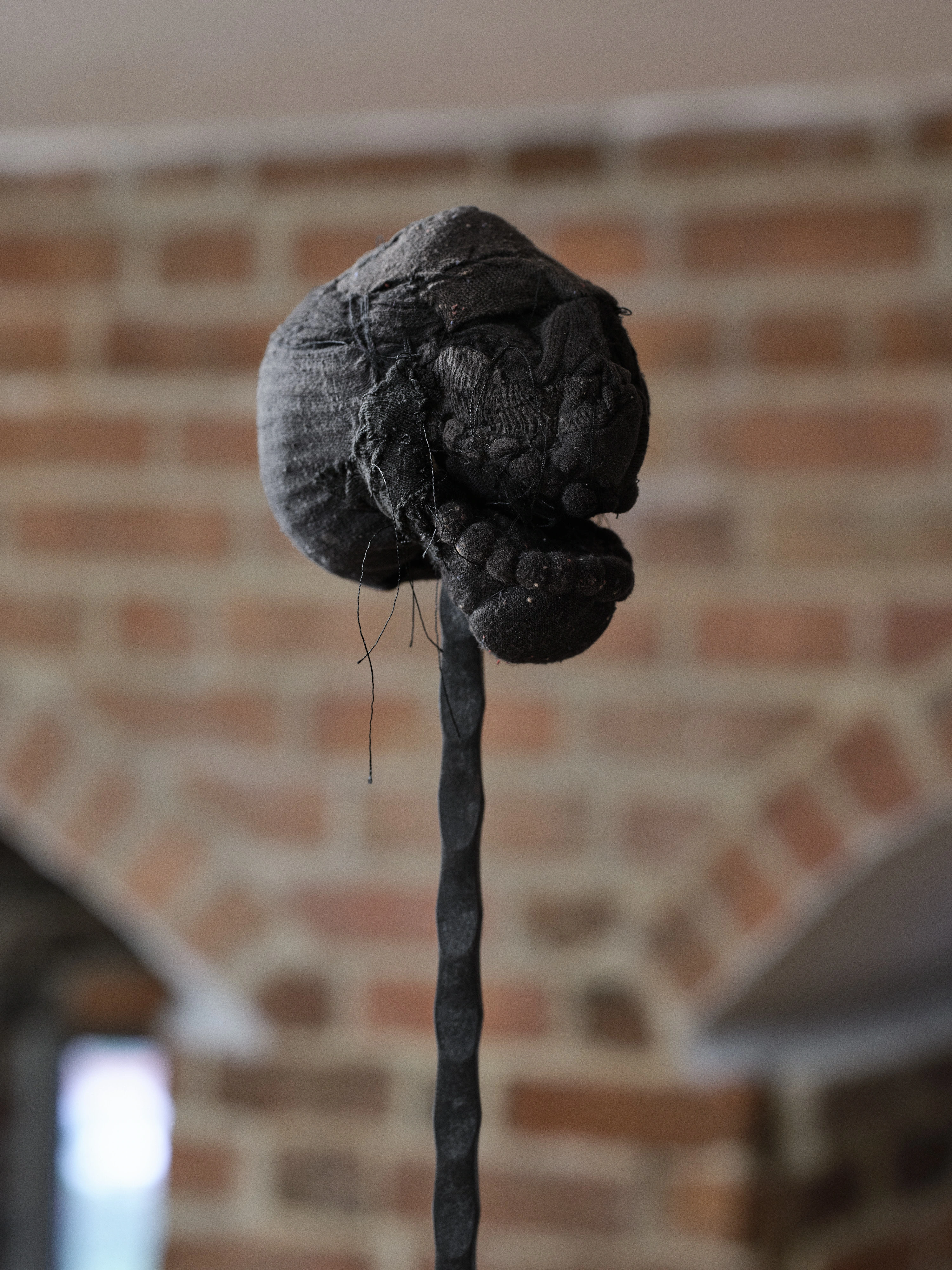 Jan Baszak, close view of Laughing Head, a small black sock head with stitched features and loose threads hanging from its jaw