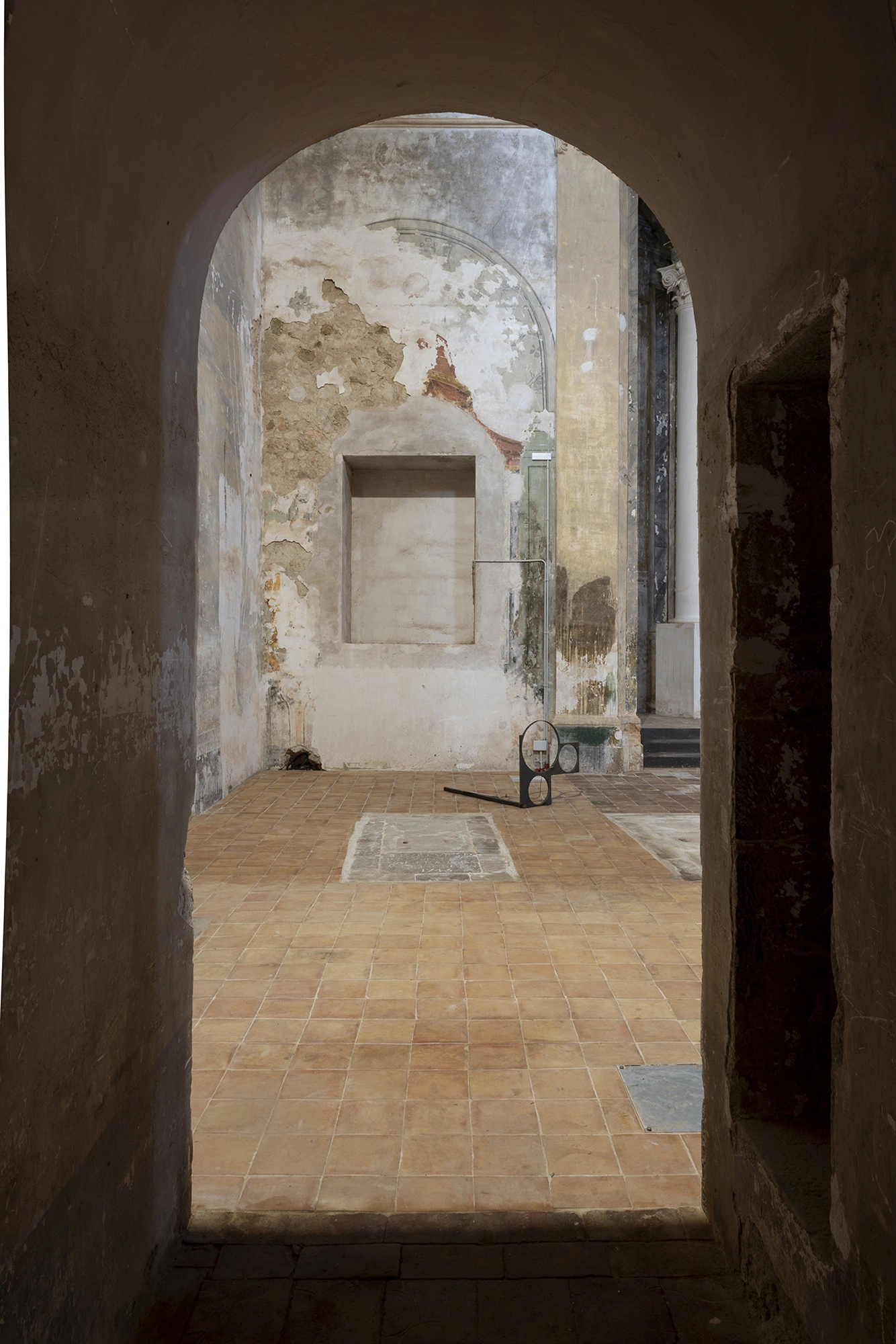 A steel sculpture by Jordi Mitjà with circular voids, seen through an arched doorway in the Church of Sant Feliu, Lladó.