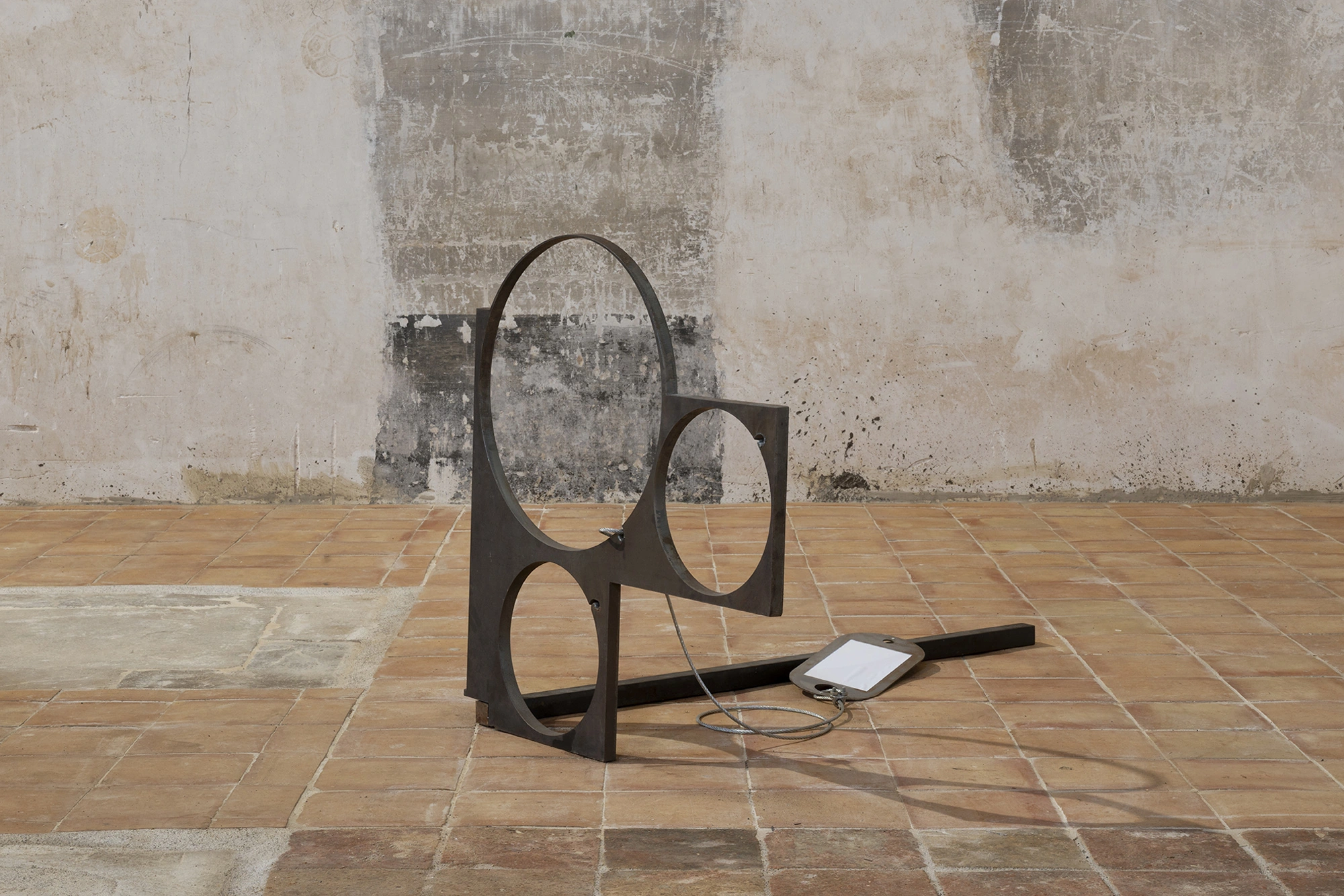 Jordi Mitjà's steel sculpture of three circular voids seen frontally on the terracotta floor, its shadow repeating the circles.