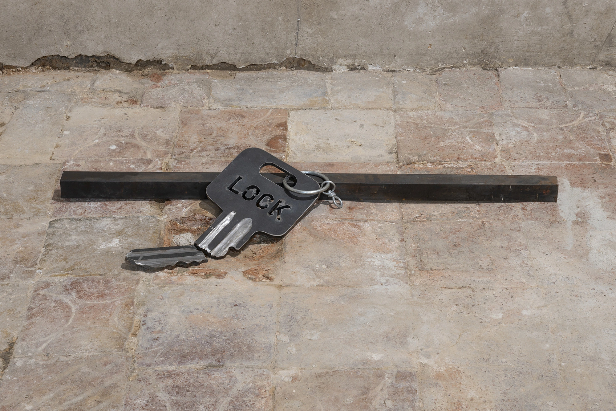 Jordi Mitjà's Clau Partida / Lock, an enlarged iron and stainless steel key, laid across an iron bar.