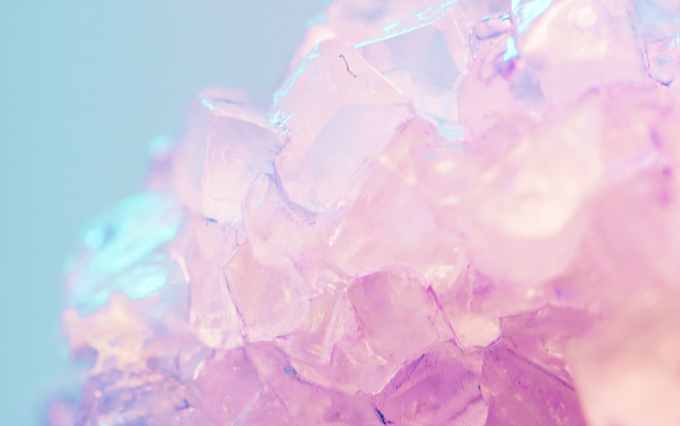 Close-up of soft pink quartz crystals with translucent, faceted edges against a pale blue background.