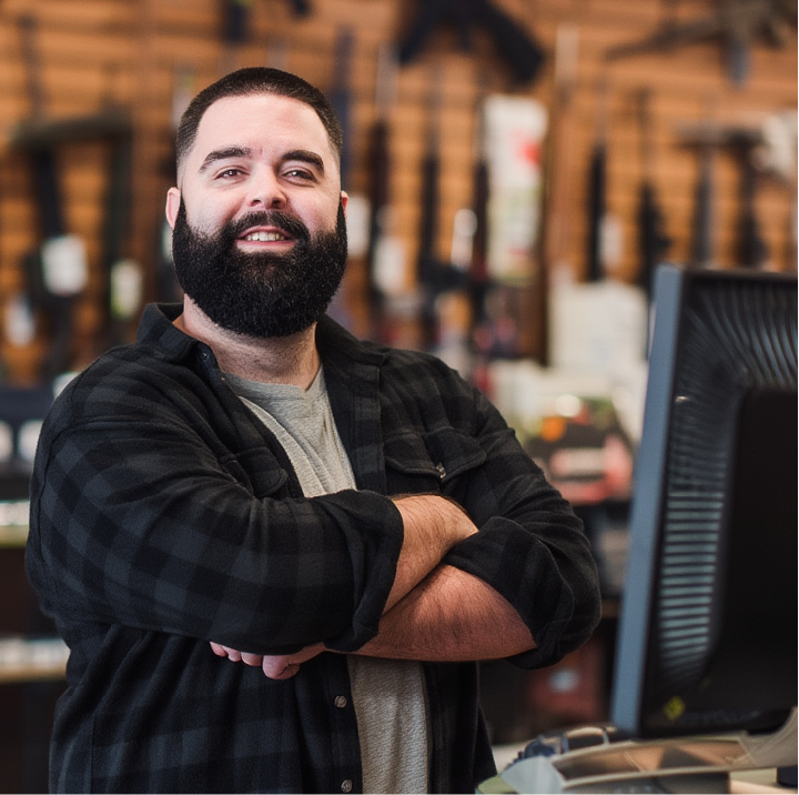 A store owner smiling crossing his arms in a gun store with a computer monitor