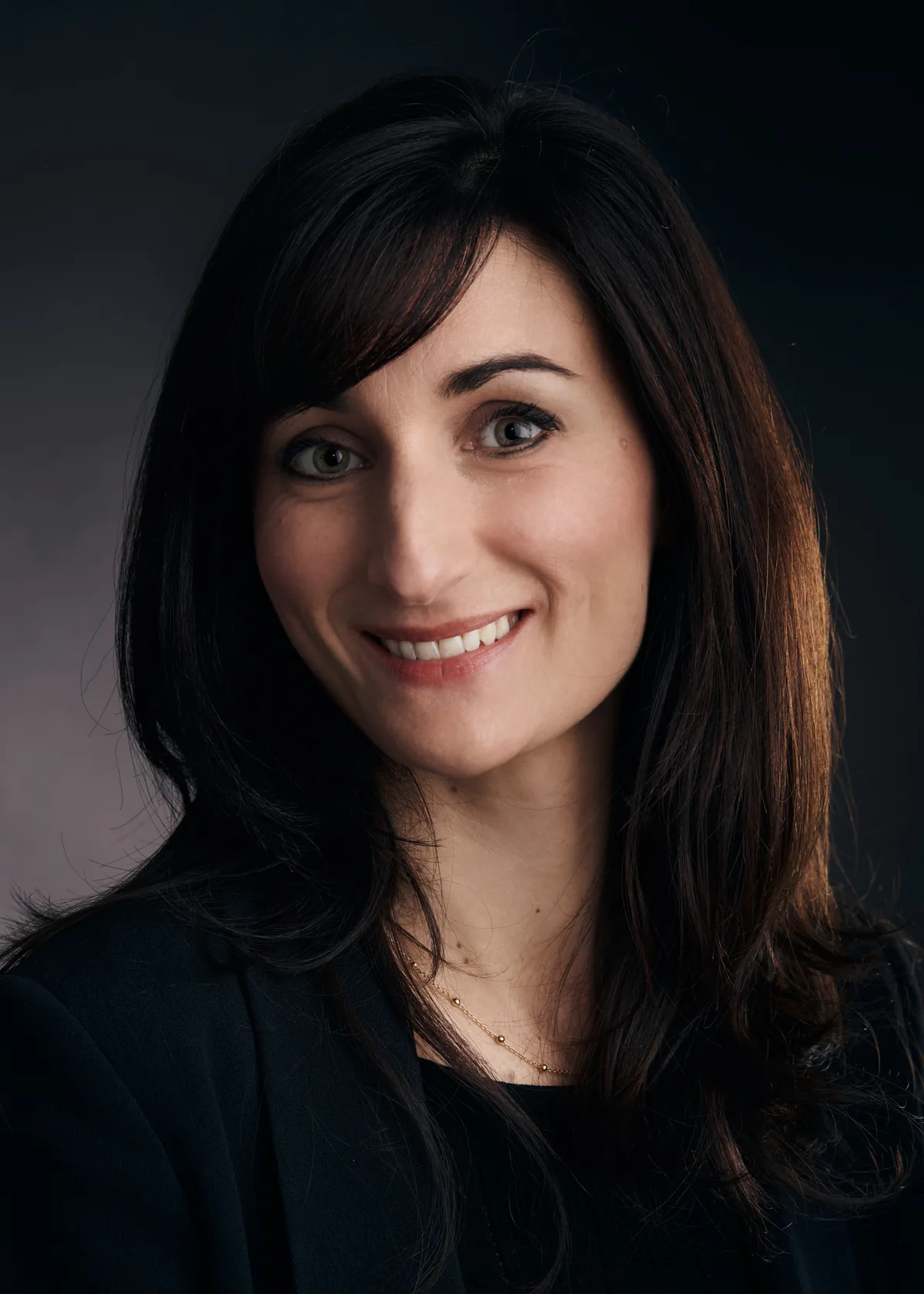 Portrait professionnel en studio d’une femme souriante sur fond sombre.