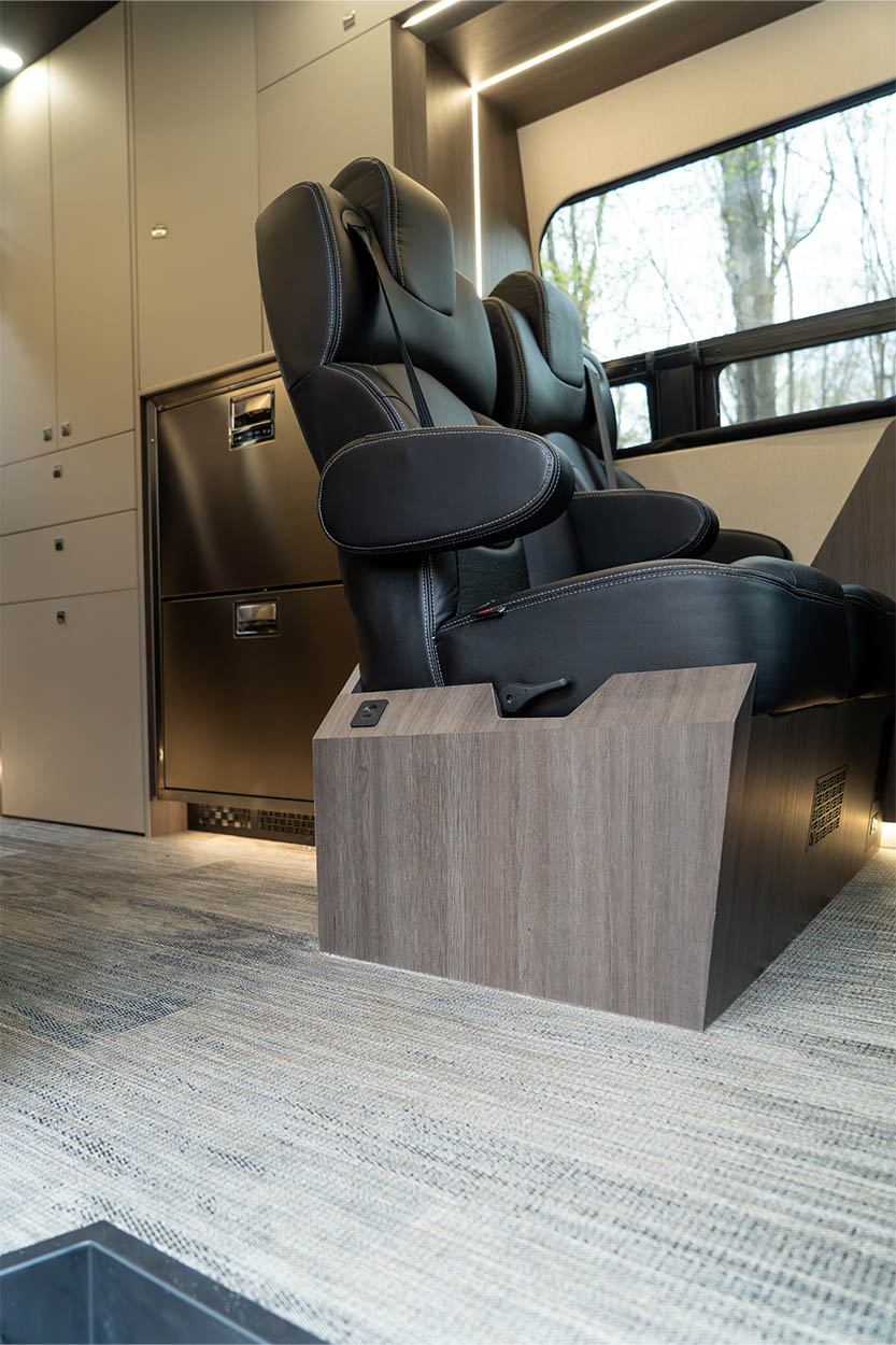Two black leather captain chairs with armrests mounted on wooden bases inside a modern RV or motorhome interior.