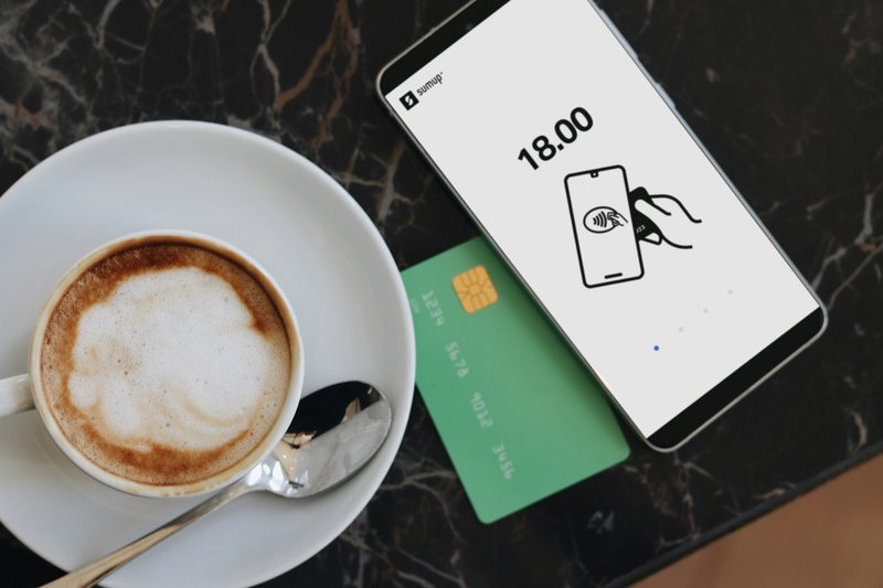 Smartphone displaying a contactless payment screen next to a coffee cup and credit card on a café table.