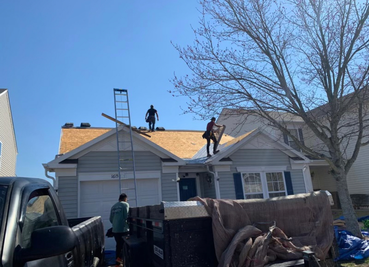 House with a trailer in the drivers and men working on the roof.