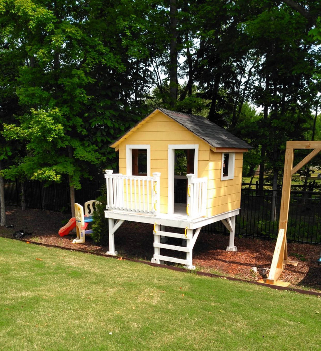 Yellow kid's playhouse with deck and roof.