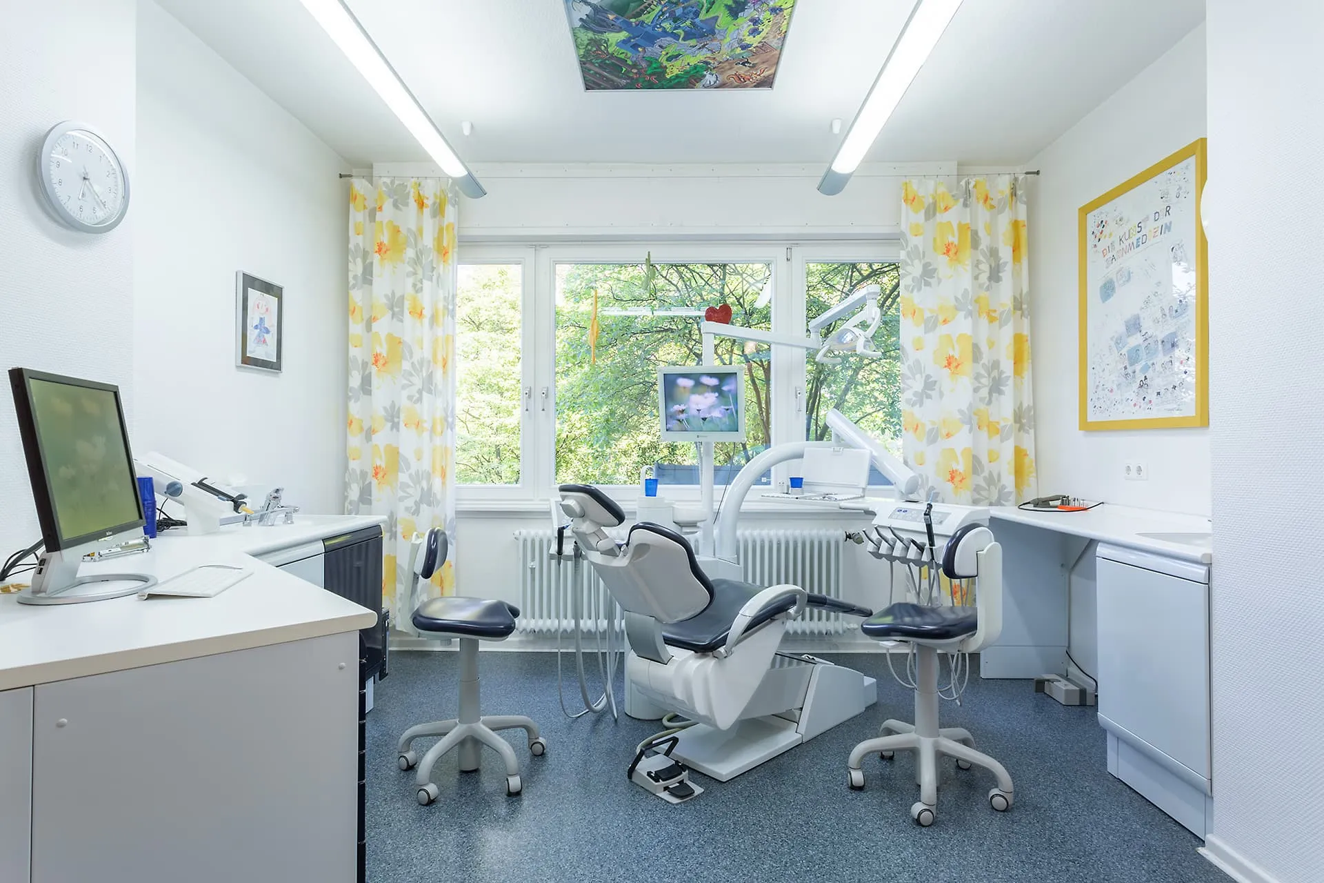 Heller Behandlungsraum mit Behandlungsstuhl, Monitor und zahnärztlichen Instrumenten, freundlich gestaltet mit gelben Vorhängen.