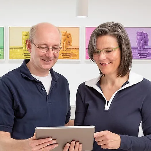 Zahnarzt und Zahnärztin (Dres. Claudia u. Lutz Klein) schauen gemeinsam auf ein Tablet im Praxisraum.