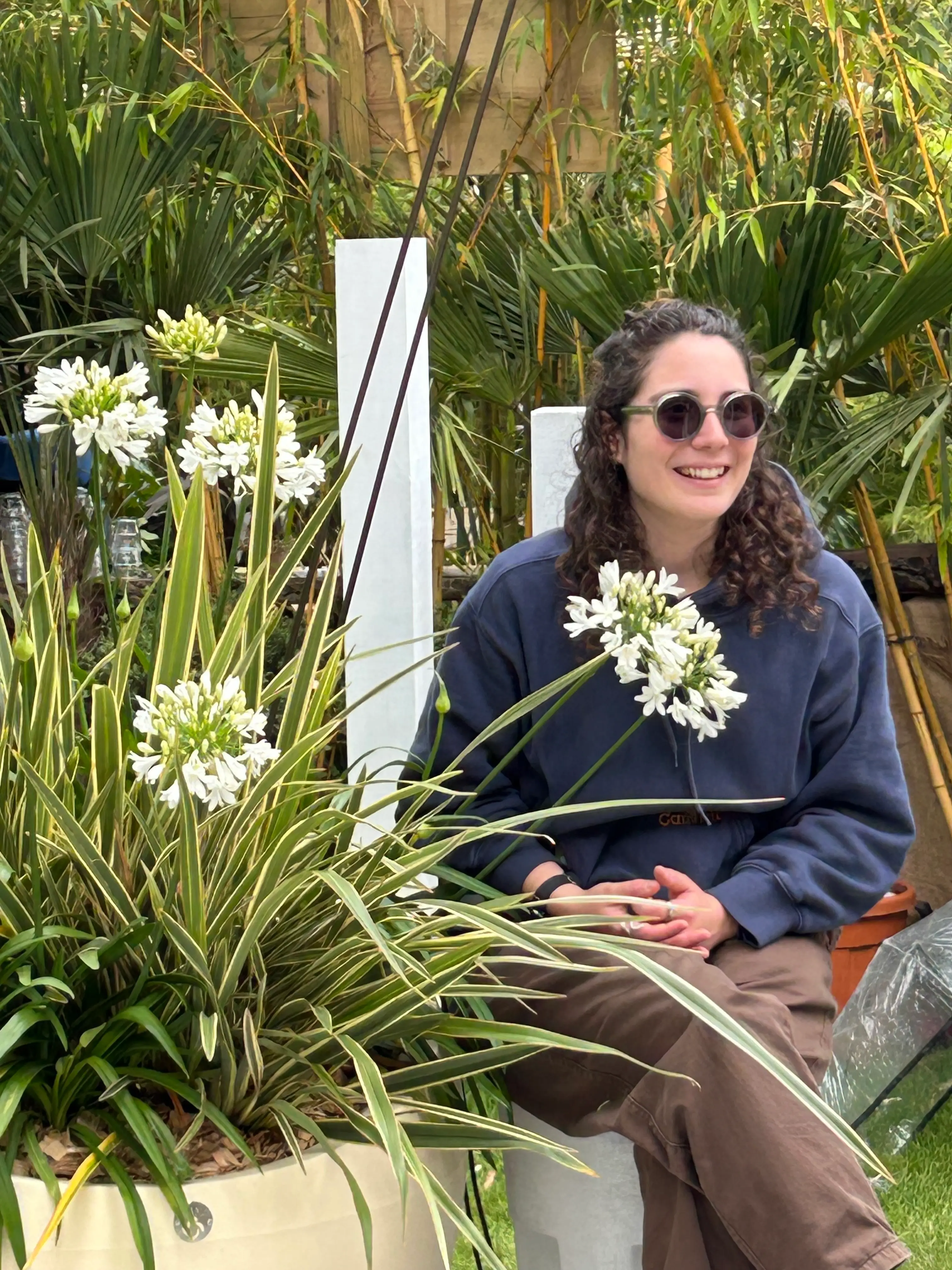 Femme souriante assise parmi des plantes vertes et des fleurs blanches