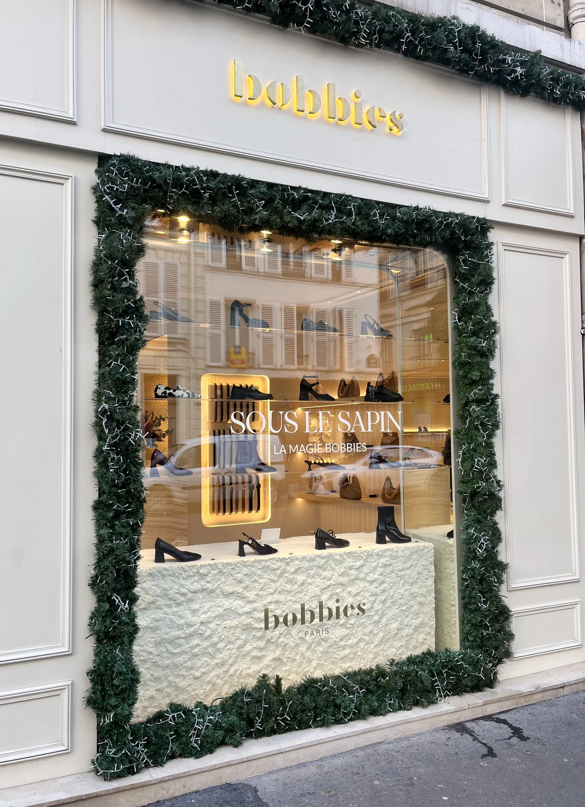Guirlande de sapin artificielle et lumineuse encadrant la vitrine d'une boutique de mode parisienne
