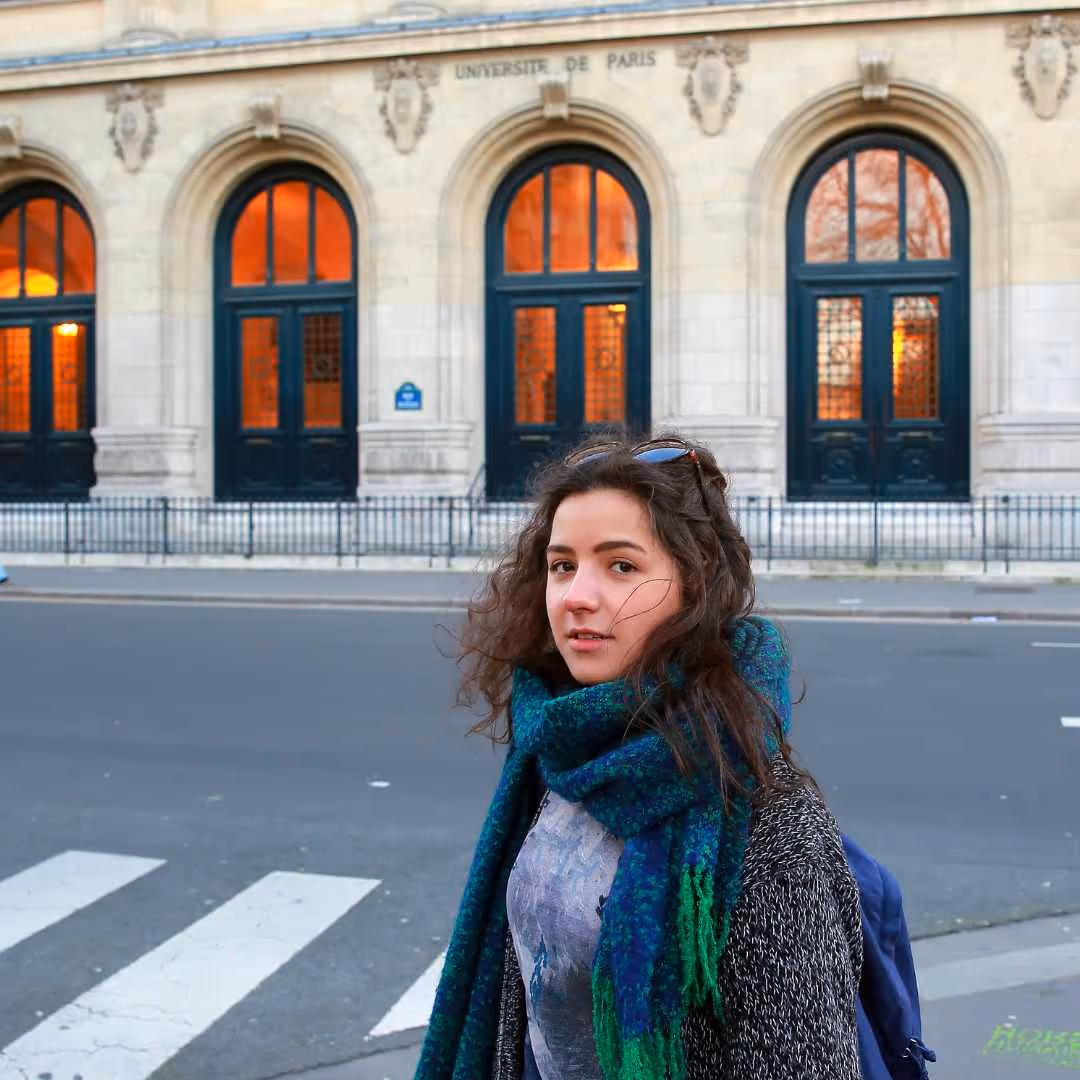 Jeune femme avec écharpe bleue et verte devant l'université de Paris à une rue piétonnière.