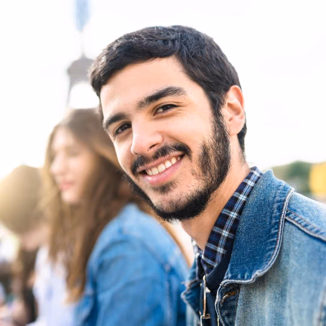 Jeune homme souriant portant une veste en jean avec des amis flous en arrière-plan.
