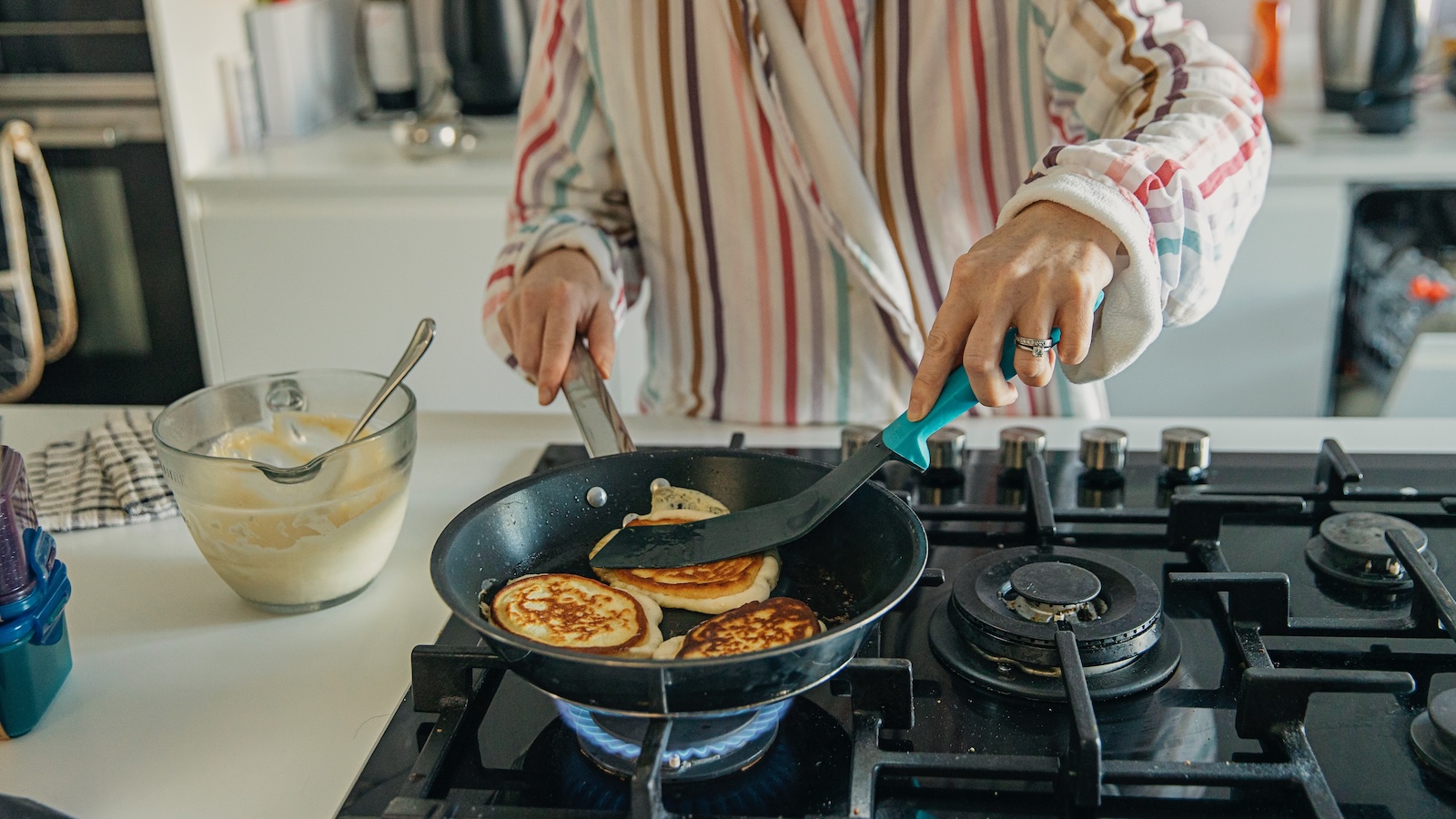 A woman is shown making pancakes in a skilled on a natural gas-burning stove.