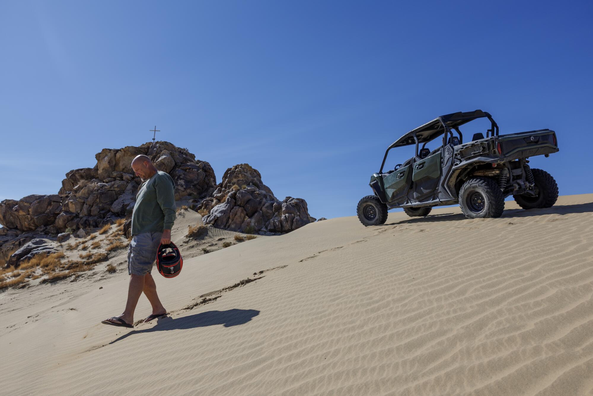 A walks on a sand dune with an off-highway vehicle in the background.