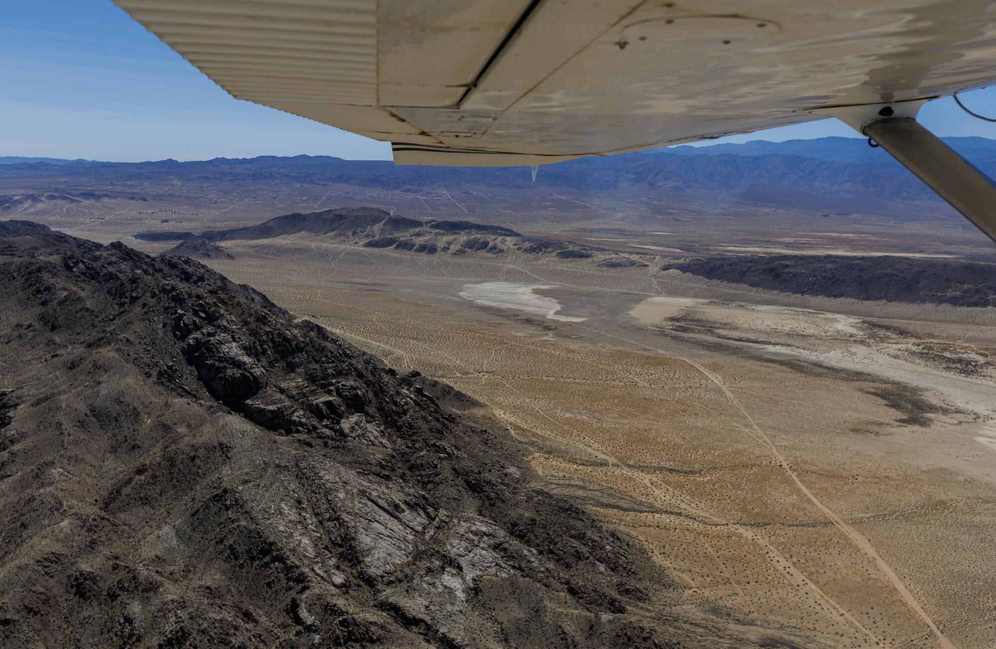 A photograph taken from inside an airplane shows a wing flying above a desert landscape.