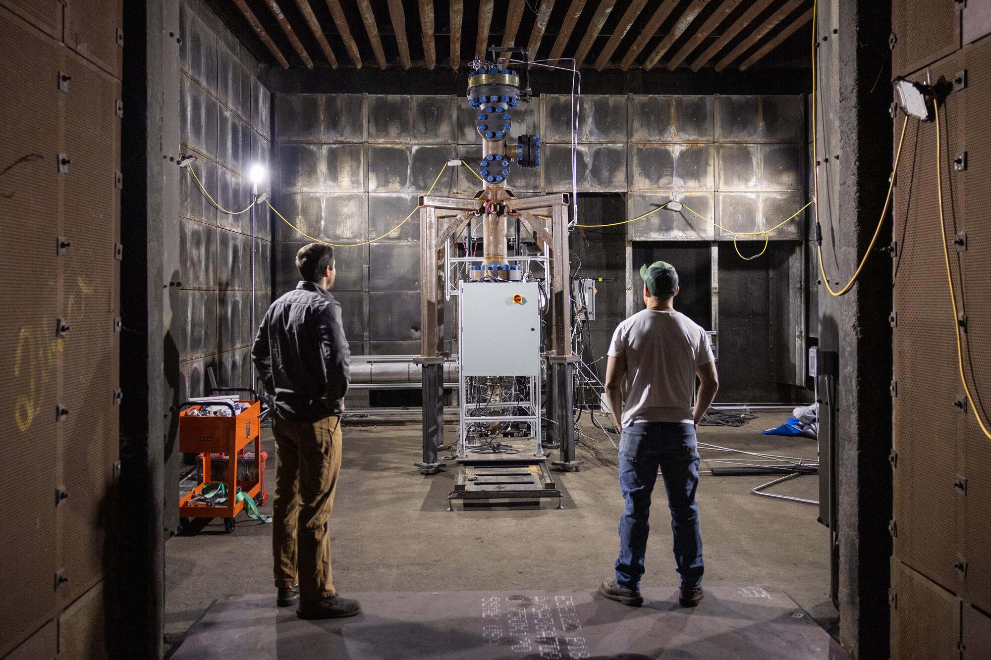 Two standing men look at a machine.