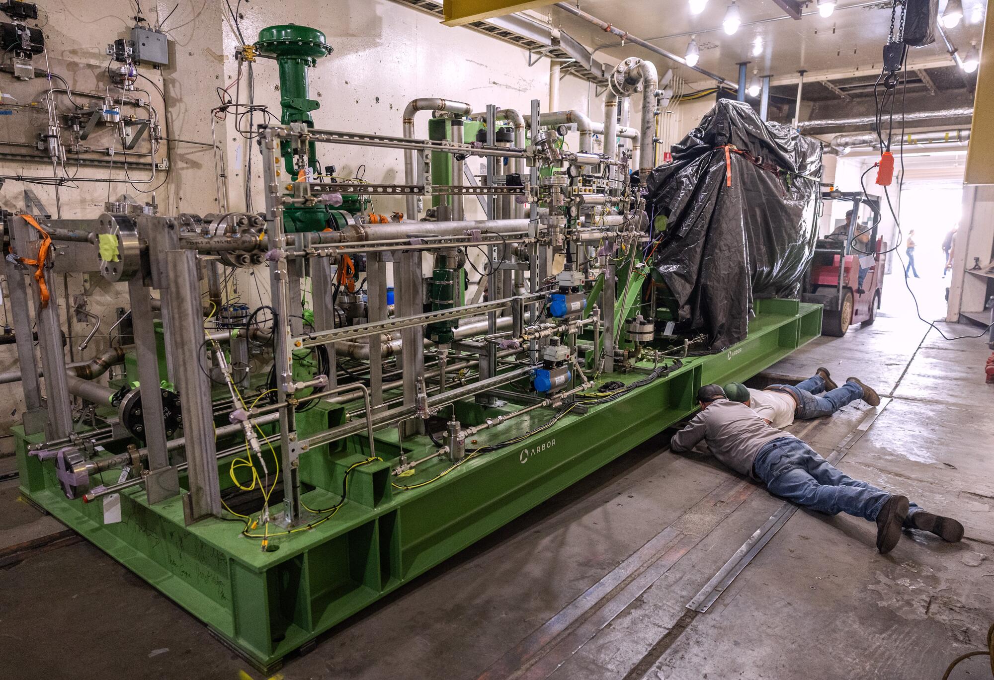 Two people crawl under machinery.