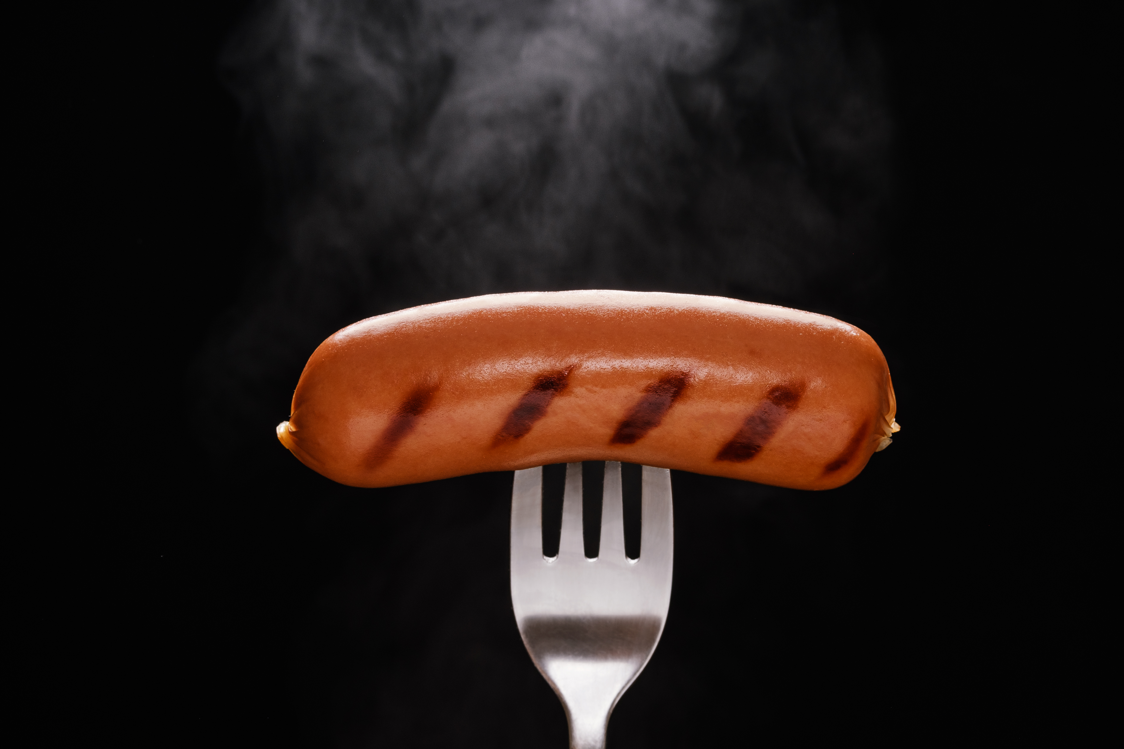 A fork with a sausage on it, with a black background.