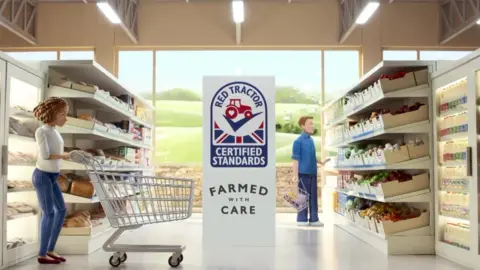 Red Tractor A screenshot of the Red Tractor advert showing an animation of a woman pushing a trolley through a supermarket, in the middle of the aisle is the Red Tractor logo underneath it says "certified standards" and "farmed with care". To the right of the image a man looks at produce on the shelves. 