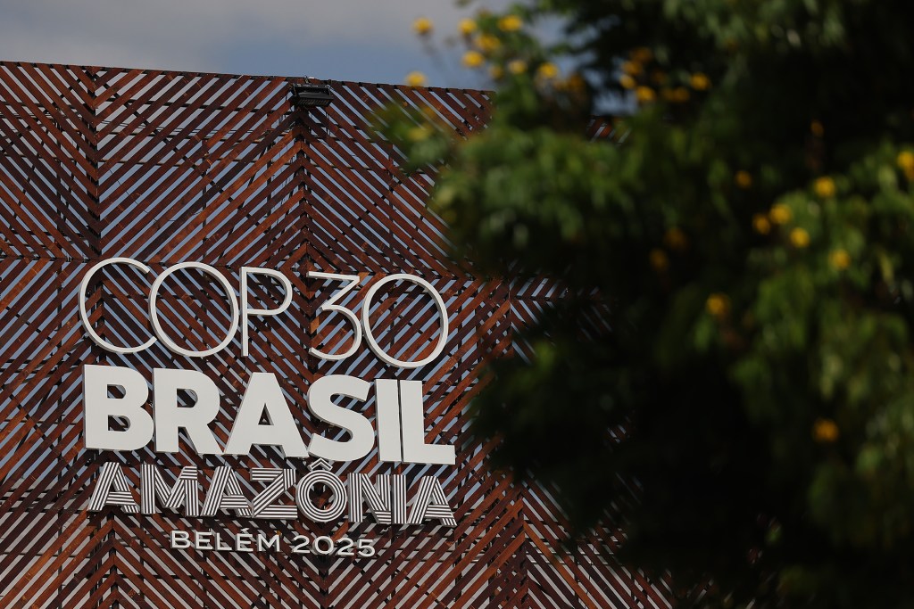 A close-up view of a white sign that reads, "COP30 Brasil Amazonia Belem 2025" set up against a brown fence structure.
