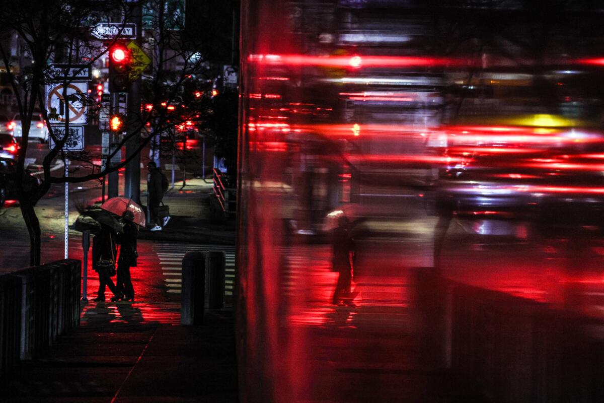 People with umbrellas walk on a city street at night.