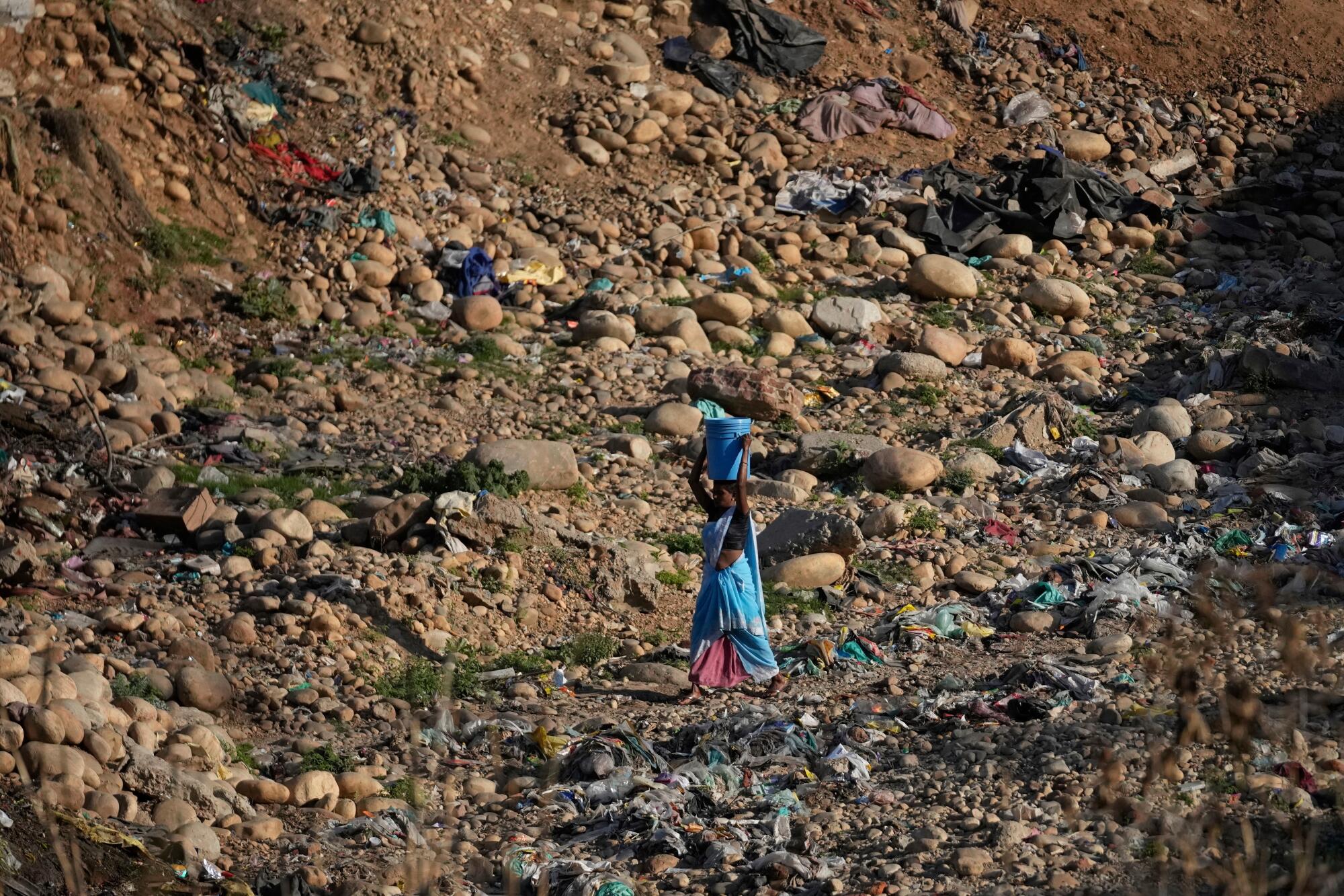 In India, a woman carries a container of drinking water filled from leaking water pipes.