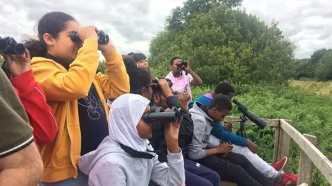 Black2Nature A group of children and teenagers bird watching. They are sitting together looking into the distance through their binoculars.