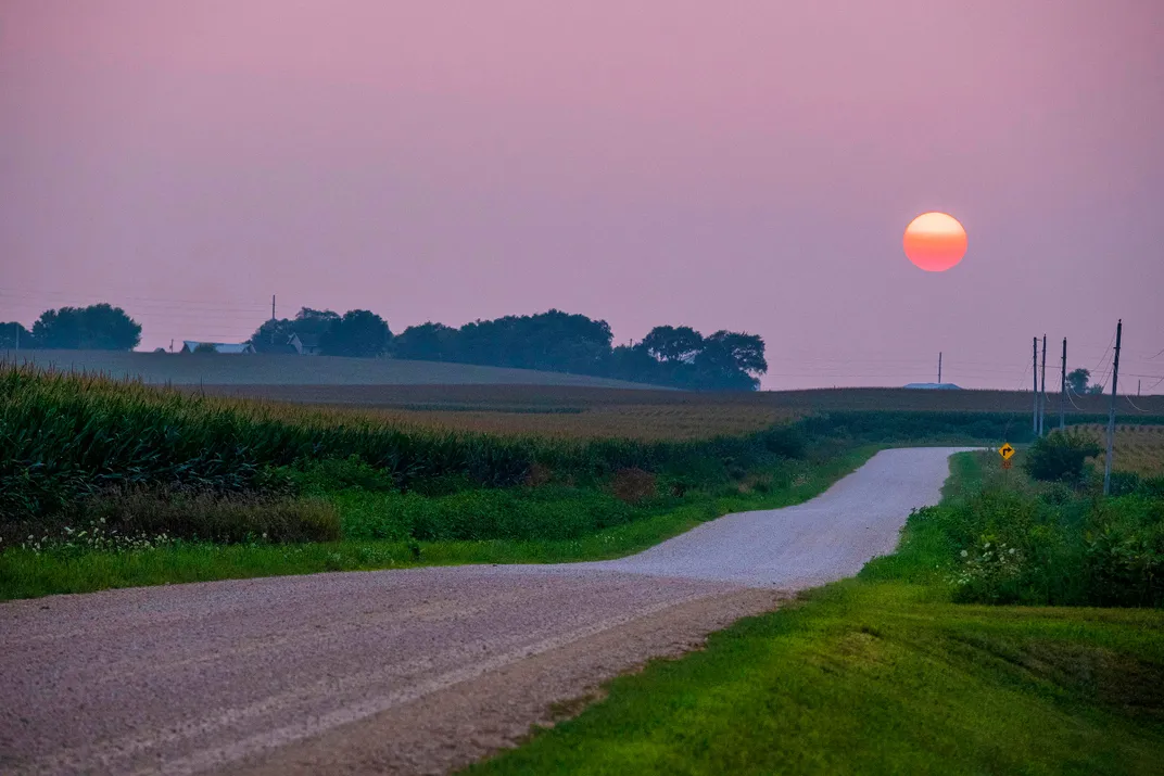 a road with the setting sun behind it and a pink sky