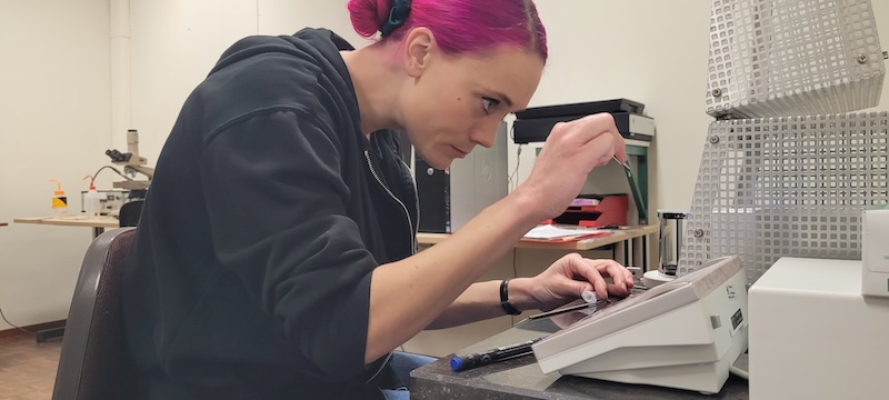 Young woman with bright pink hair pulled back sitting in front of desktop equipment.