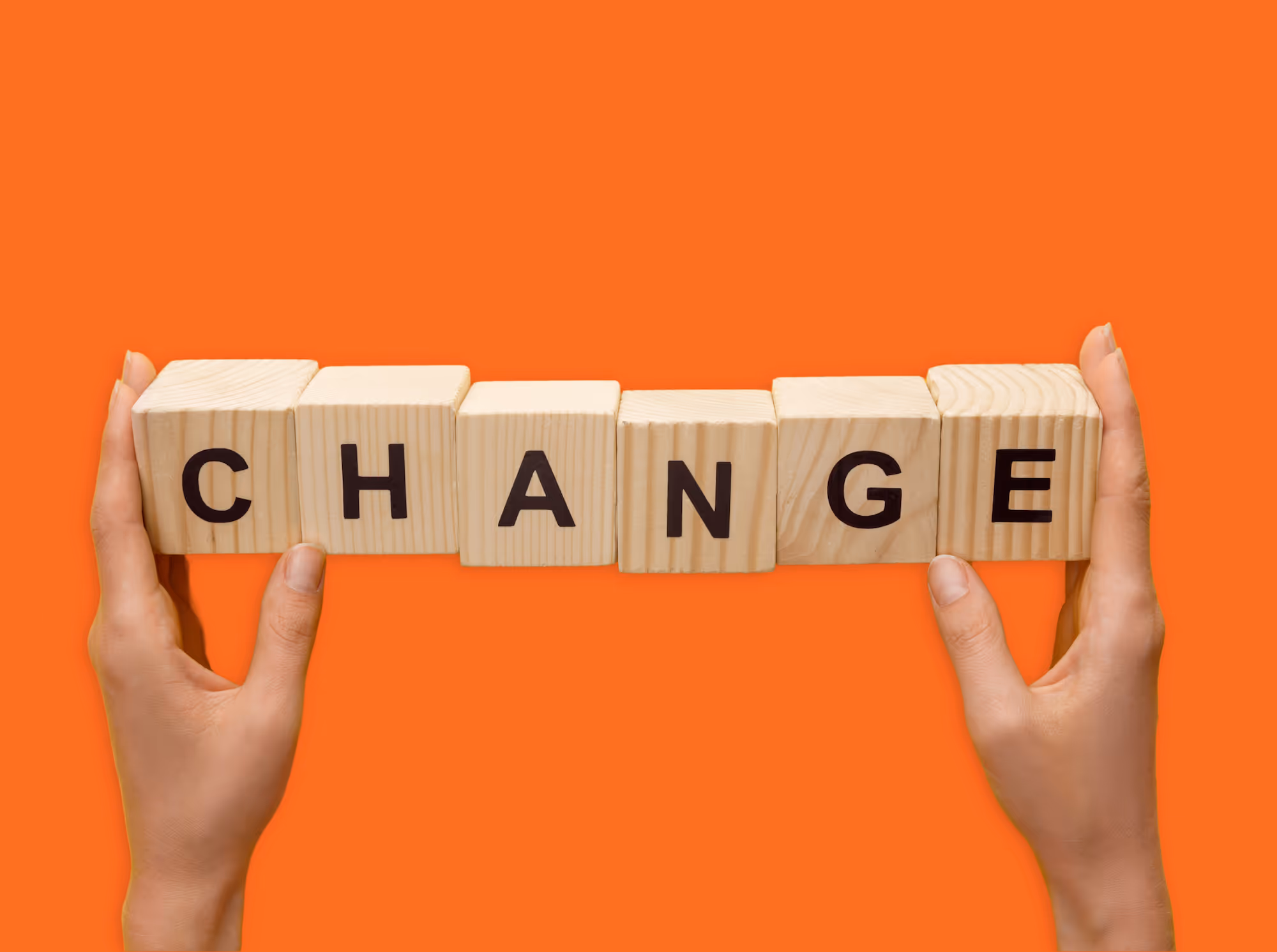 Two hands holding wooden blocks spelling out "CHANGE" on a bright orange background.
