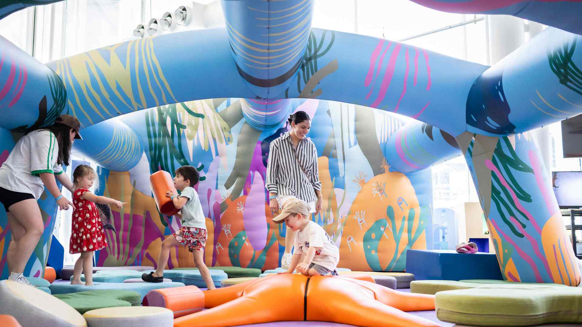 Children playing inside a colourful inflatable play structure with an adult supervising.