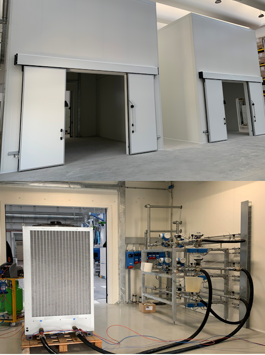 Two large white climate test chambers with open doors in a clean industrial setting, alongside control valves and pipes connected to a large ventilation or cooling unit on a wooden pallet.