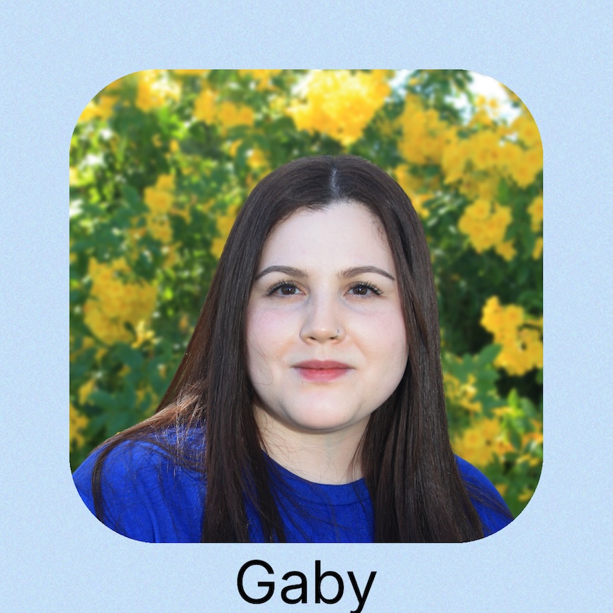 A woman wearing a blue shirt with logo stands in front of a serene water 