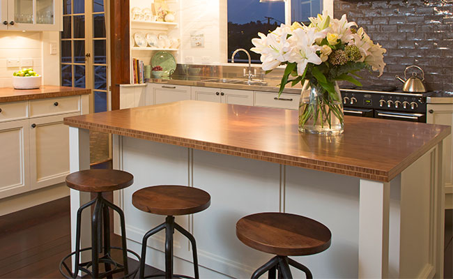 Tan bamboo kitchen island countertop, with white cabinet unit and matching bamboo and steel stools