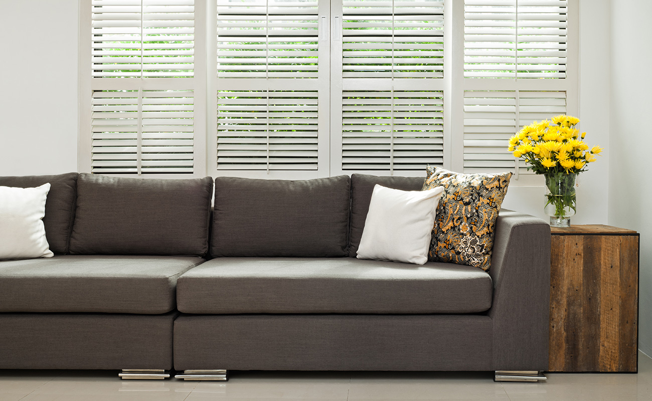A living room couch sits under a window with wooden frames