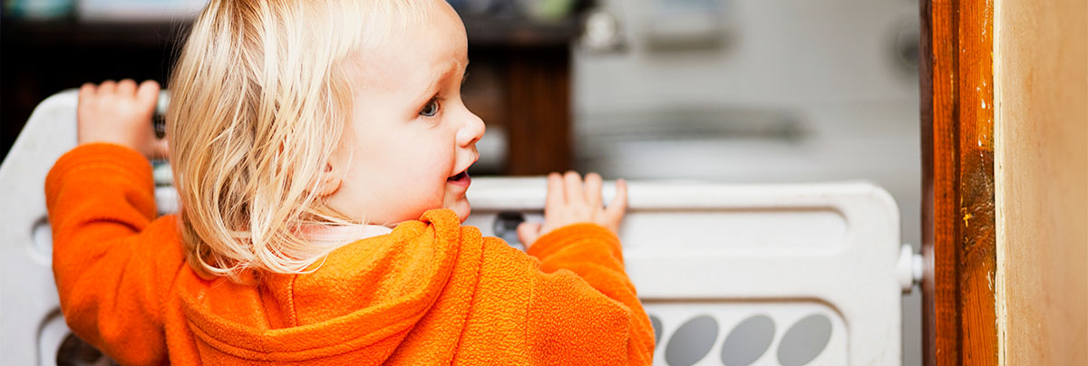 Toddler standing at child safety gate looking back over his shoulder