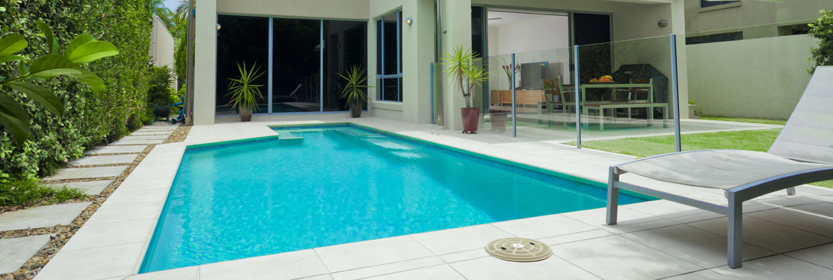 Outdoor, in ground, backyard swimming pool with glass panel fencing