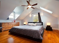 A well lit and ventilated bedroom, with a wide window, high ceiling and a ceiling fan.