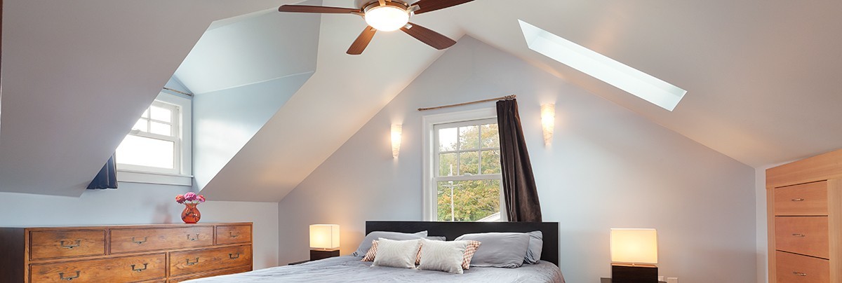 A well lit and ventilated bedroom, with a wide window, high ceiling and a ceiling fan.