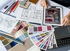 Designer working on colour schemes and architectural plans with the help of a tablet and a computer