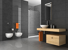 Renovated bathroom with different shades of grey paneling with glass enclosed shower and white vanity and toilet.