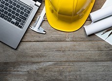 Wooden table with a yellow construction helmet, laptop and plans