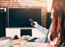 A lady was using a remote to open the TV