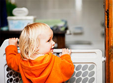 Toddler standing at child safety gate looking back over his shoulder