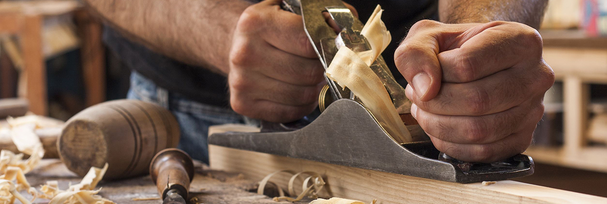 Man scrapping off old wood from surface to reupholster.