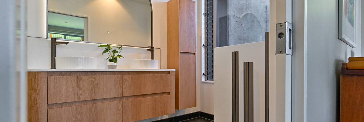 bathroom with wooden cabinets and two sinks under a half circle mirror