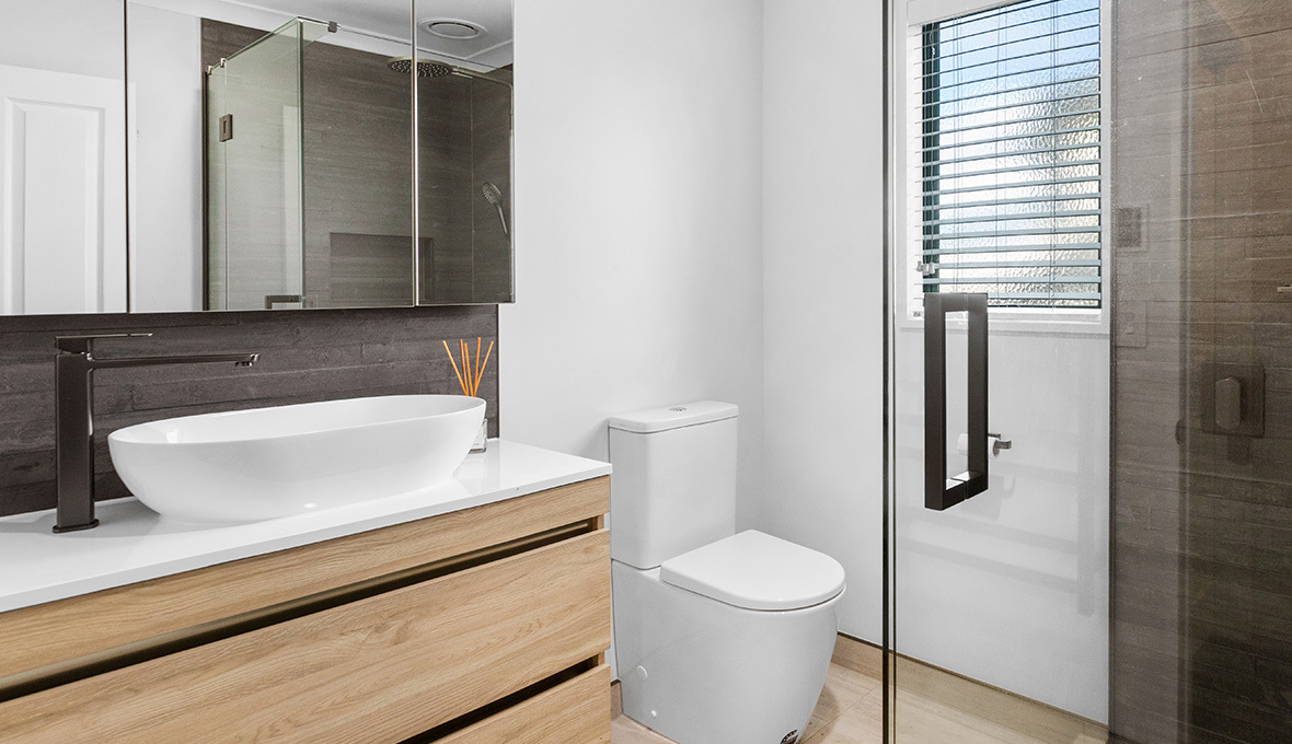 Timaru bathroom renovation featuring a wood vanity, glass fittings, and a white basin sink.