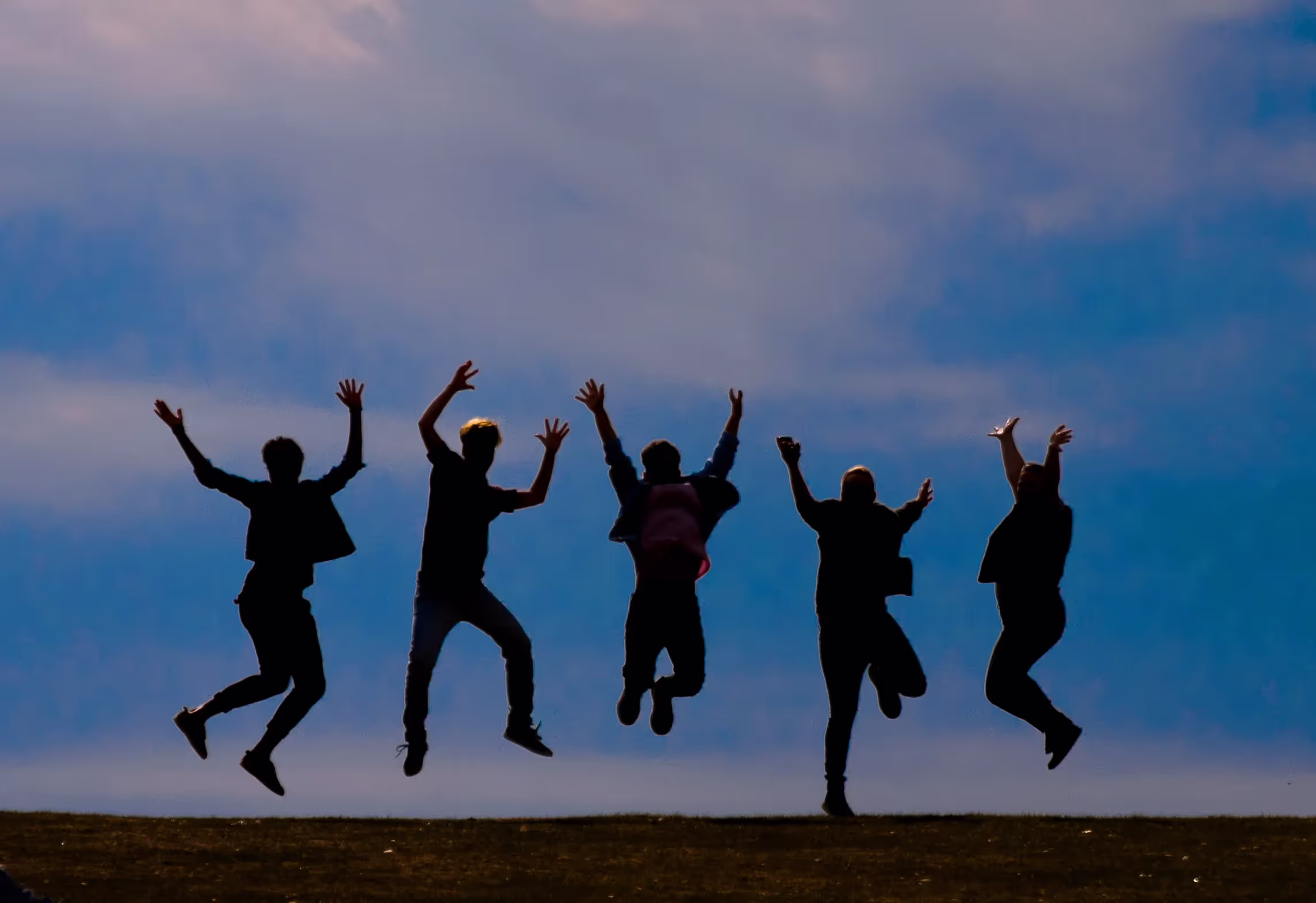 Das Bild zeigt fünf Personen, von denen man nur die Umrisse erkennen kann, wie sie in die Luft springen. Im Hintergrund sieht man den Himmel mit einigen Wolken.
