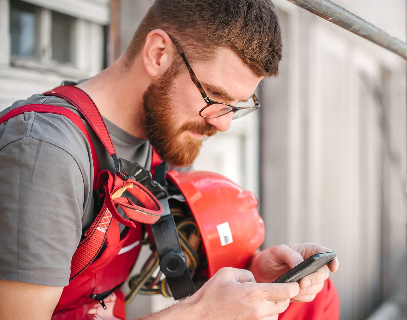Smiling construction worker in safety gear, looking at his phone with a relaxed expression.